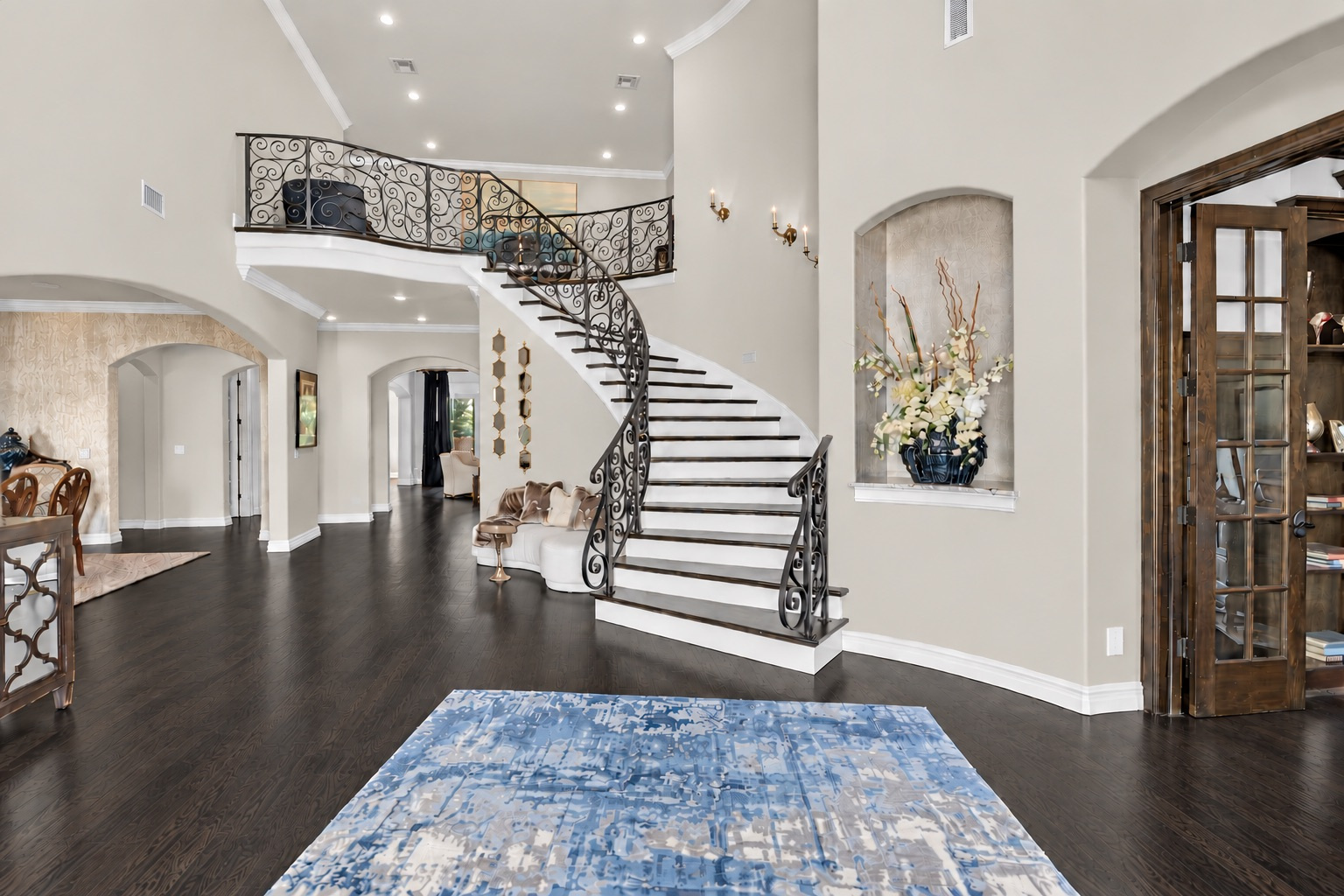 Foyer with a sweeping wrought-iron staircase, dark wood floors, and a two-story ceiling.