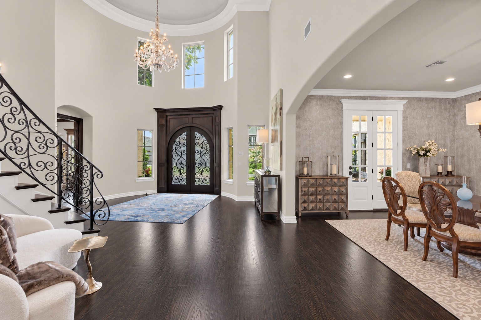 Two-story foyer with an ornate double front door, chandelier, curved staircase, and adjoining dining room.