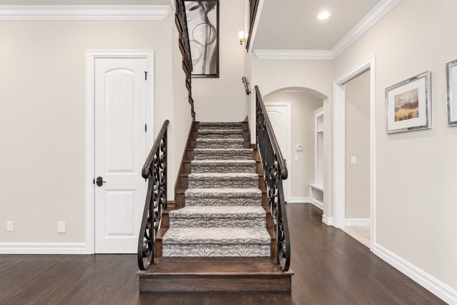 Foyer staircase with patterned carpet, dark wood steps, and ornate iron railings.