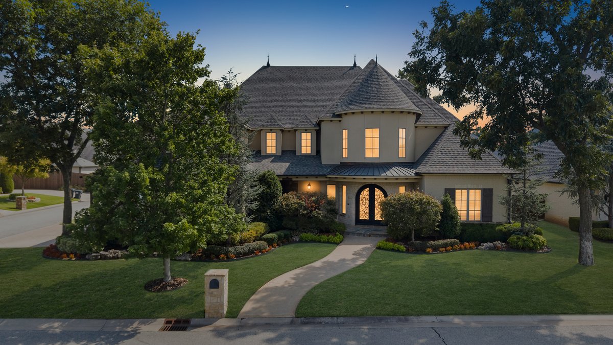 Two-story home with a rounded turret, glowing windows, mature trees, and a curved front walkway at dusk.