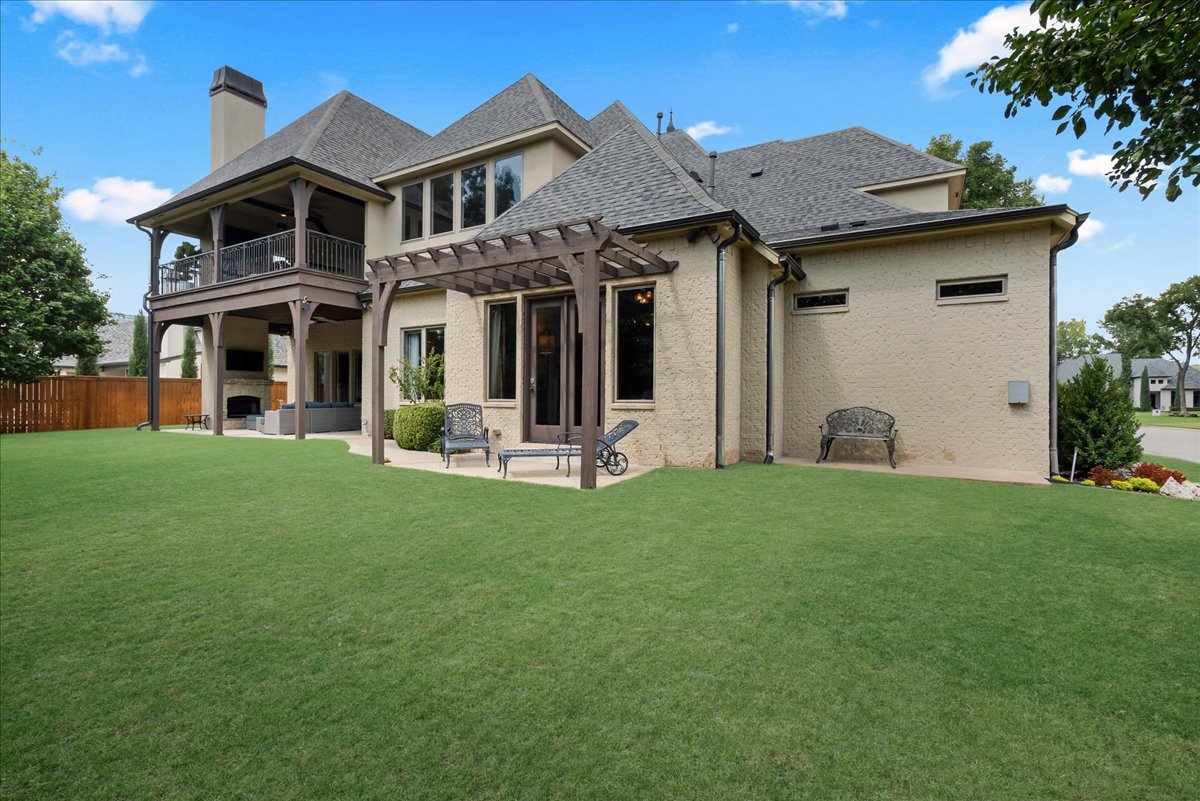 Beige brick home with a covered balcony, pergola, and broad green lawn.
