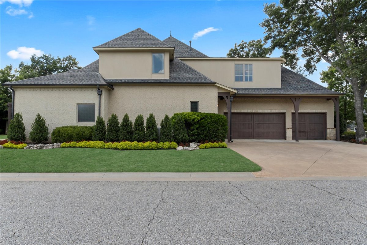 Two-story beige stucco home with two garage doors, landscaped front yard, and wide driveway.