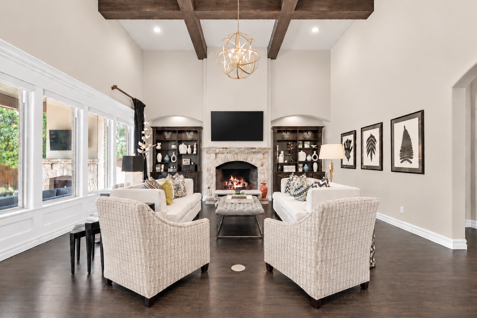 Living room with a stone fireplace, tall windows, exposed wood beams, and white seating.