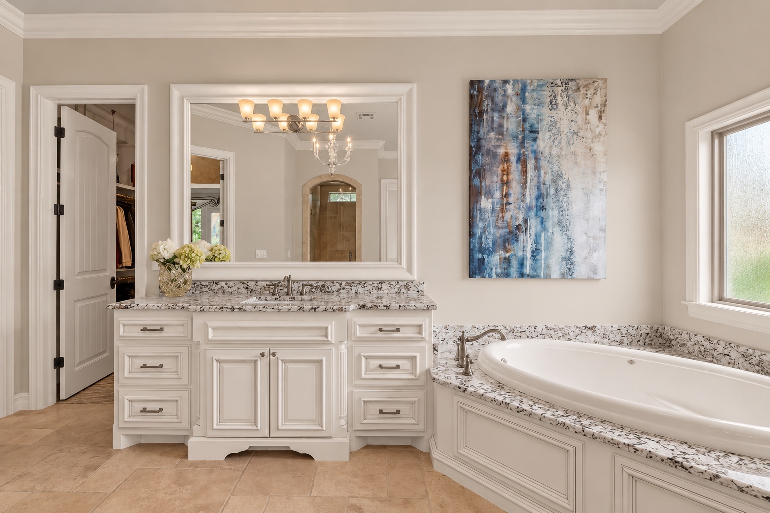 Primary bathroom with a white vanity and granite counters beside a built-in soaking tub under a window.
