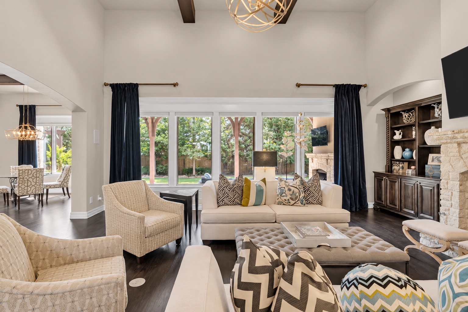 Furnished living room with tall backyard-facing windows, a stone fireplace, and a built-in display cabinet.