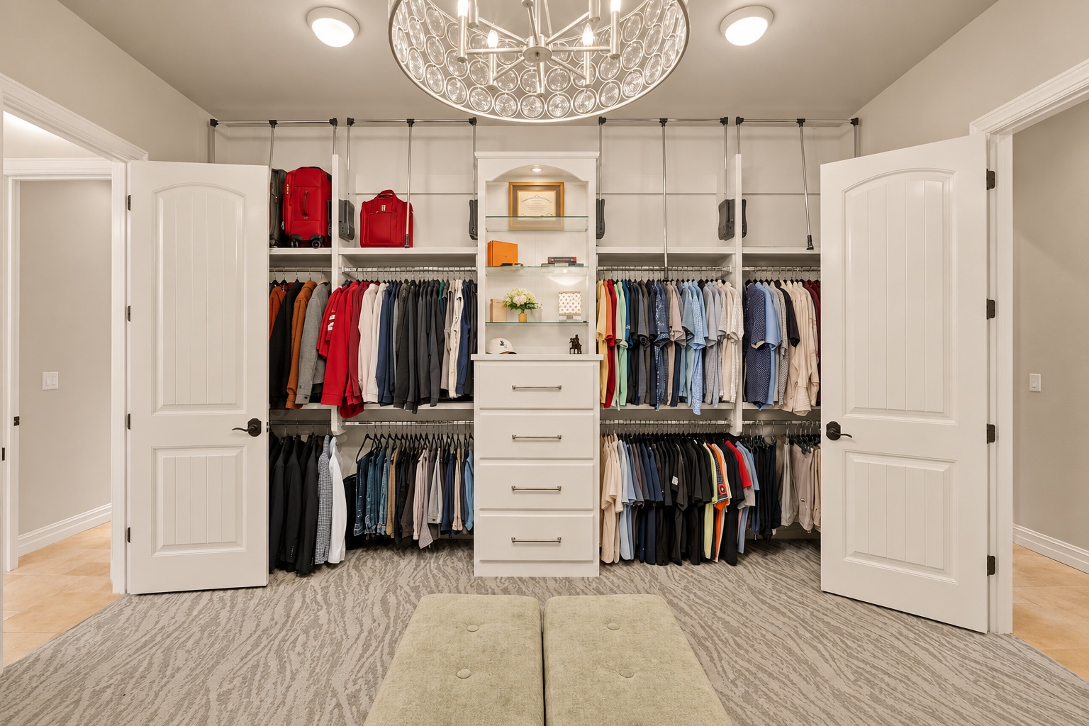 Walk-in closet with extensive clothing storage, central drawers, and an ornate chandelier.