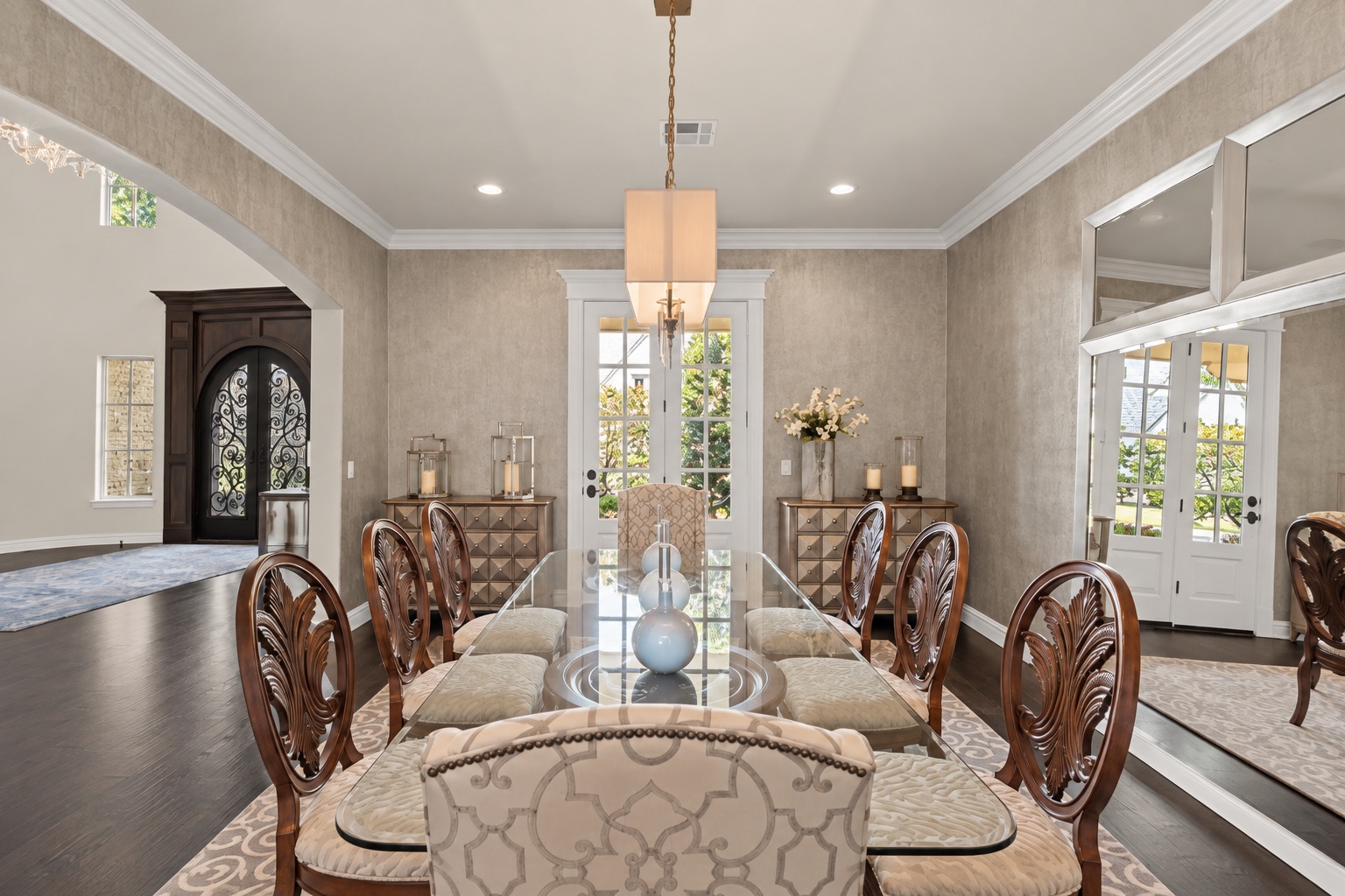 Dining room with a glass-top table, carved wooden chairs, and a hanging chandelier.