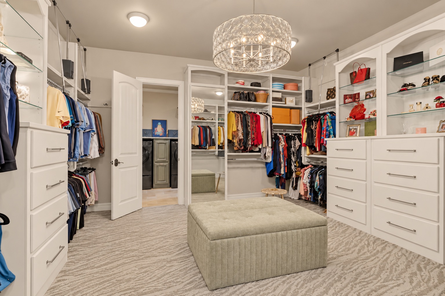 Walk-in closet with built-in drawers, clothing racks, glass shelves, and a large upholstered ottoman.