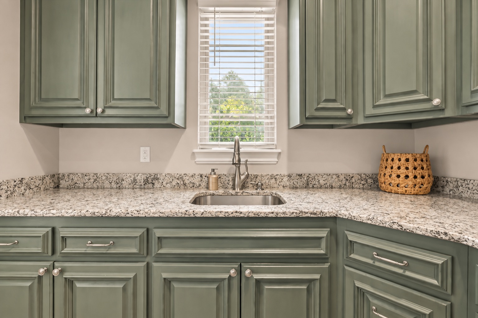 Kitchen with sage-green cabinets, speckled granite counters, and a sink beneath a window.
