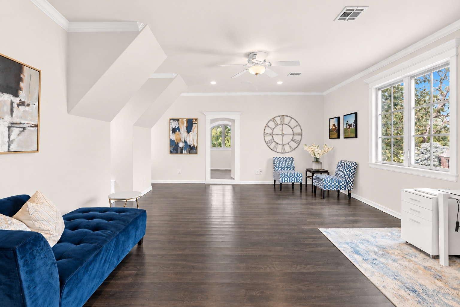 Living room with a blue velvet sofa, patterned armchairs, dark wood floors, and wide windows.