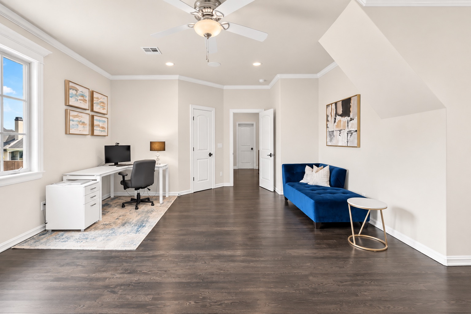Furnished home office with a white desk by the window and a blue loveseat against the opposite wall.