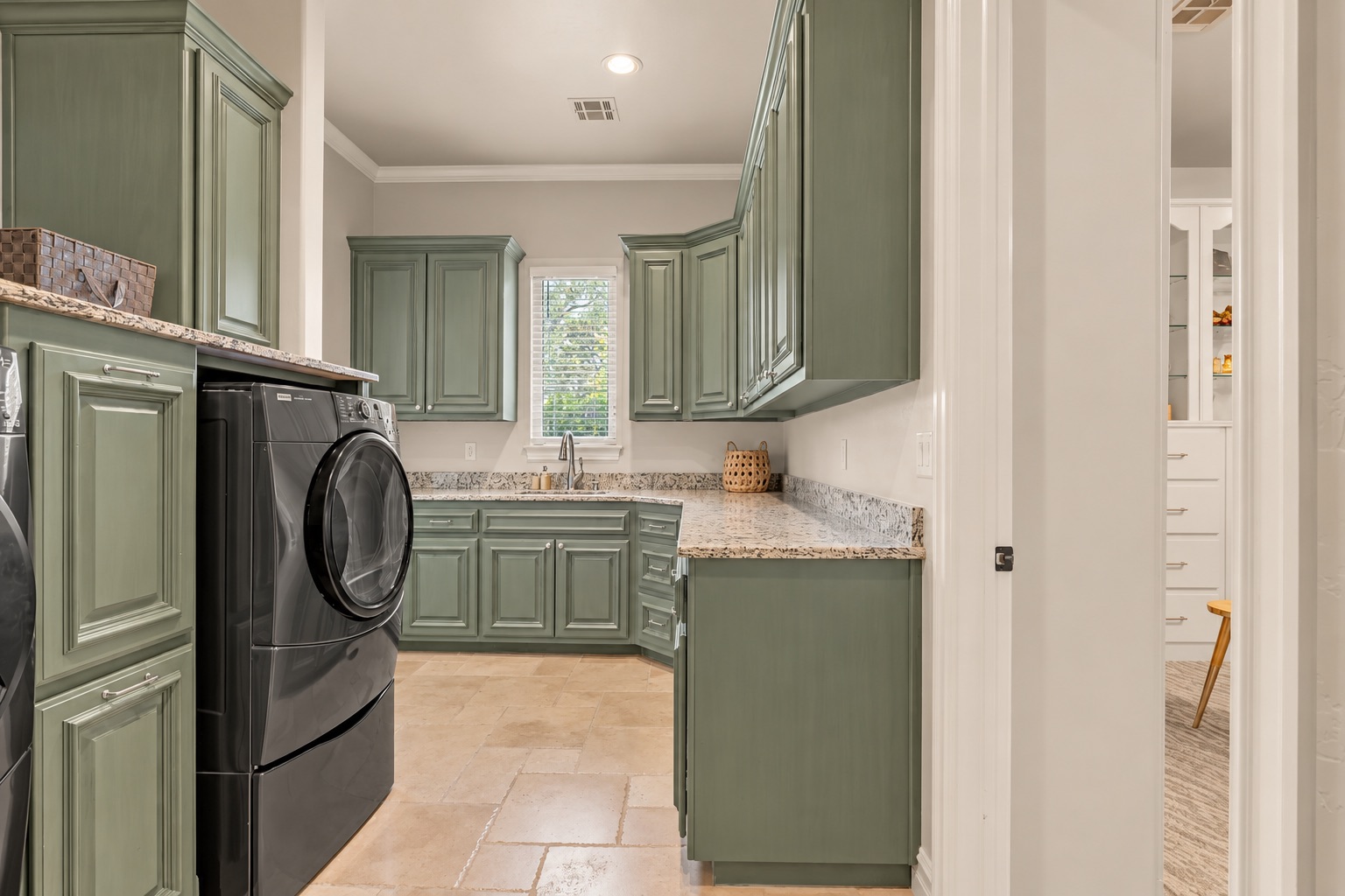 Laundry room with sage-green cabinetry, granite counters, and black front-loading washer and dryer.