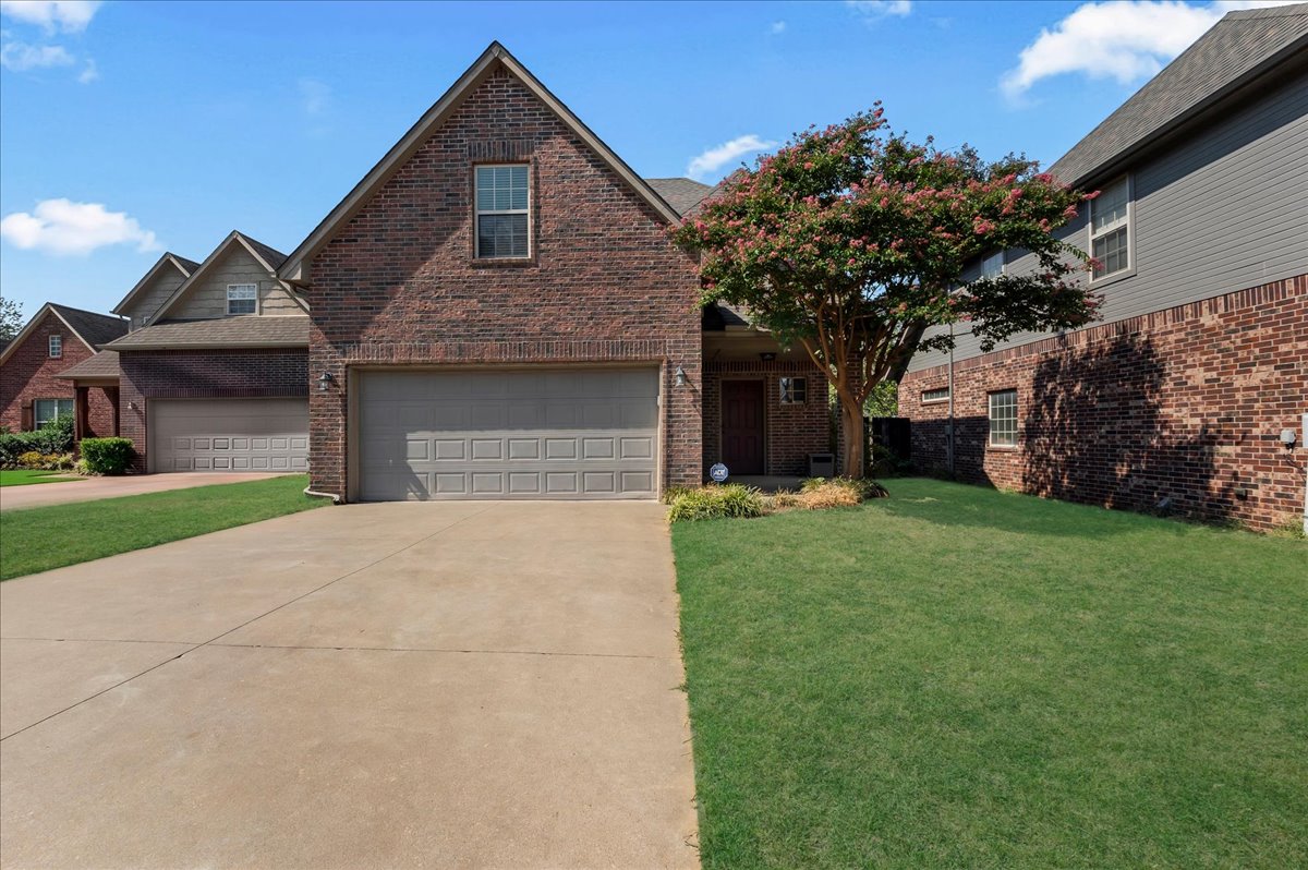 Brick two-story home with a two-car garage, concrete driveway, and flowering tree by the entrance.
