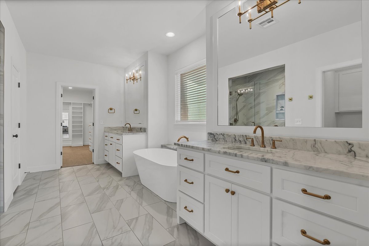 Primary bathroom with a freestanding tub, marble double vanity, and marble-look tile floors.