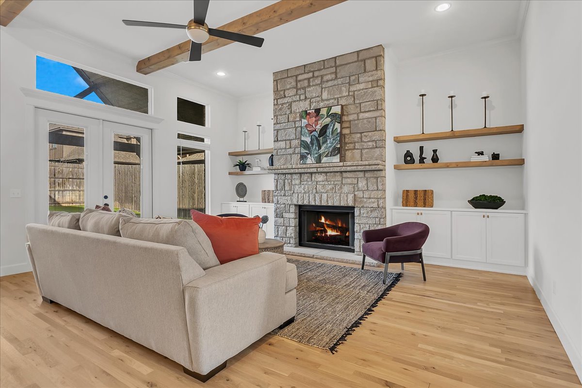 Staged living room with a stone fireplace, exposed ceiling beams, and large glass doors.