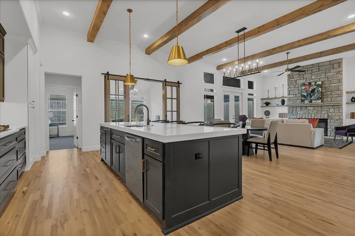Open-plan kitchen with a large charcoal island, exposed wood beams, and a stone fireplace.