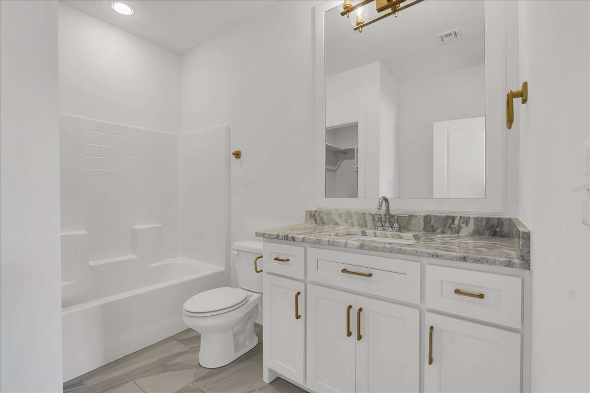 Bathroom with a white tub, gray veined stone vanity, and gold-tone hardware.