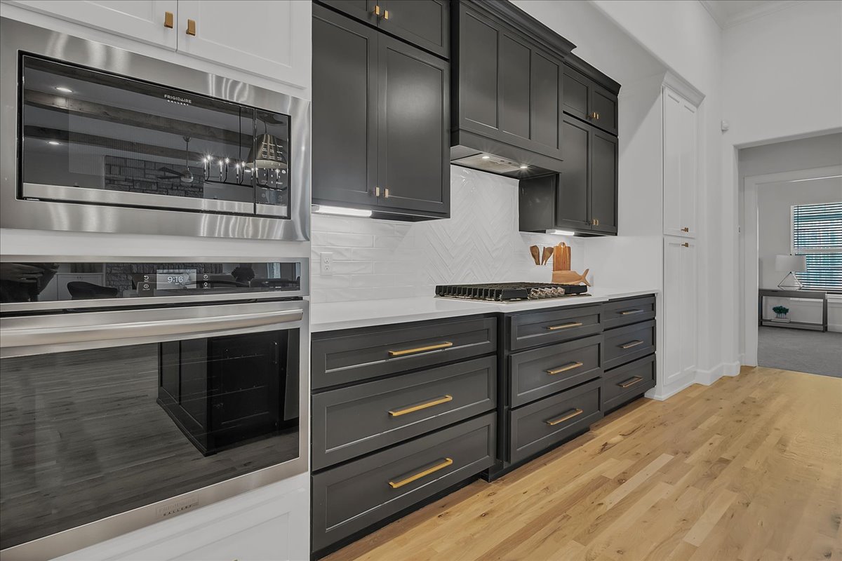 Modern kitchen with charcoal cabinets, stainless double ovens, a gas cooktop, and light hardwood floors.