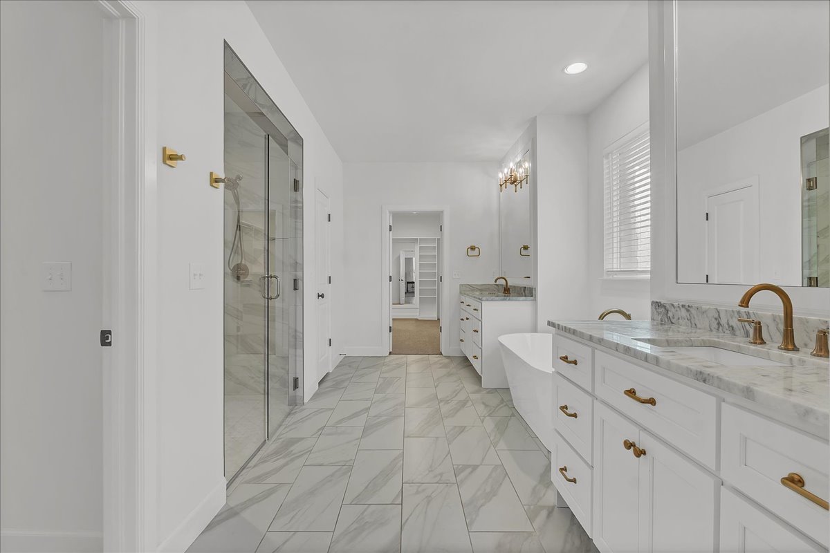 Bathroom with a glass shower, freestanding tub, and marble vanity with brass fixtures.