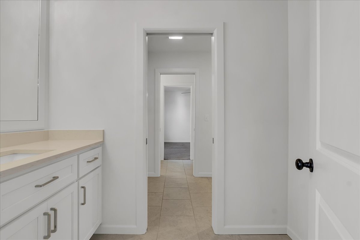 Bathroom vanity beside a tiled passage leading through aligned doorways to a carpeted room.