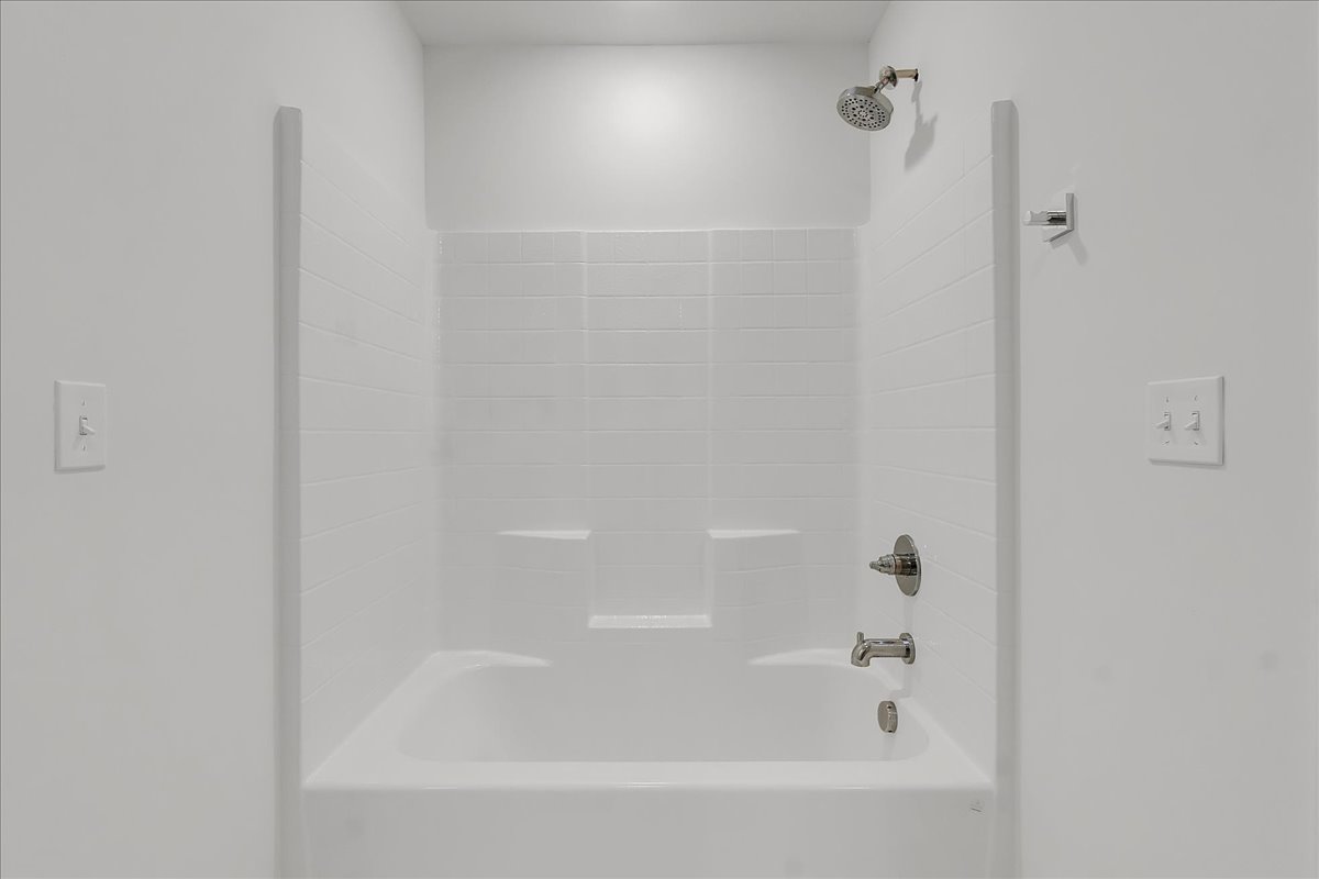 White bathtub and shower with built-in shelves and chrome fixtures.