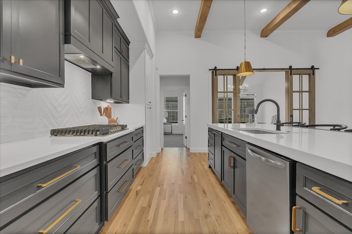 Modern kitchen with charcoal cabinets, white counters, wood beams, and sliding barn doors.