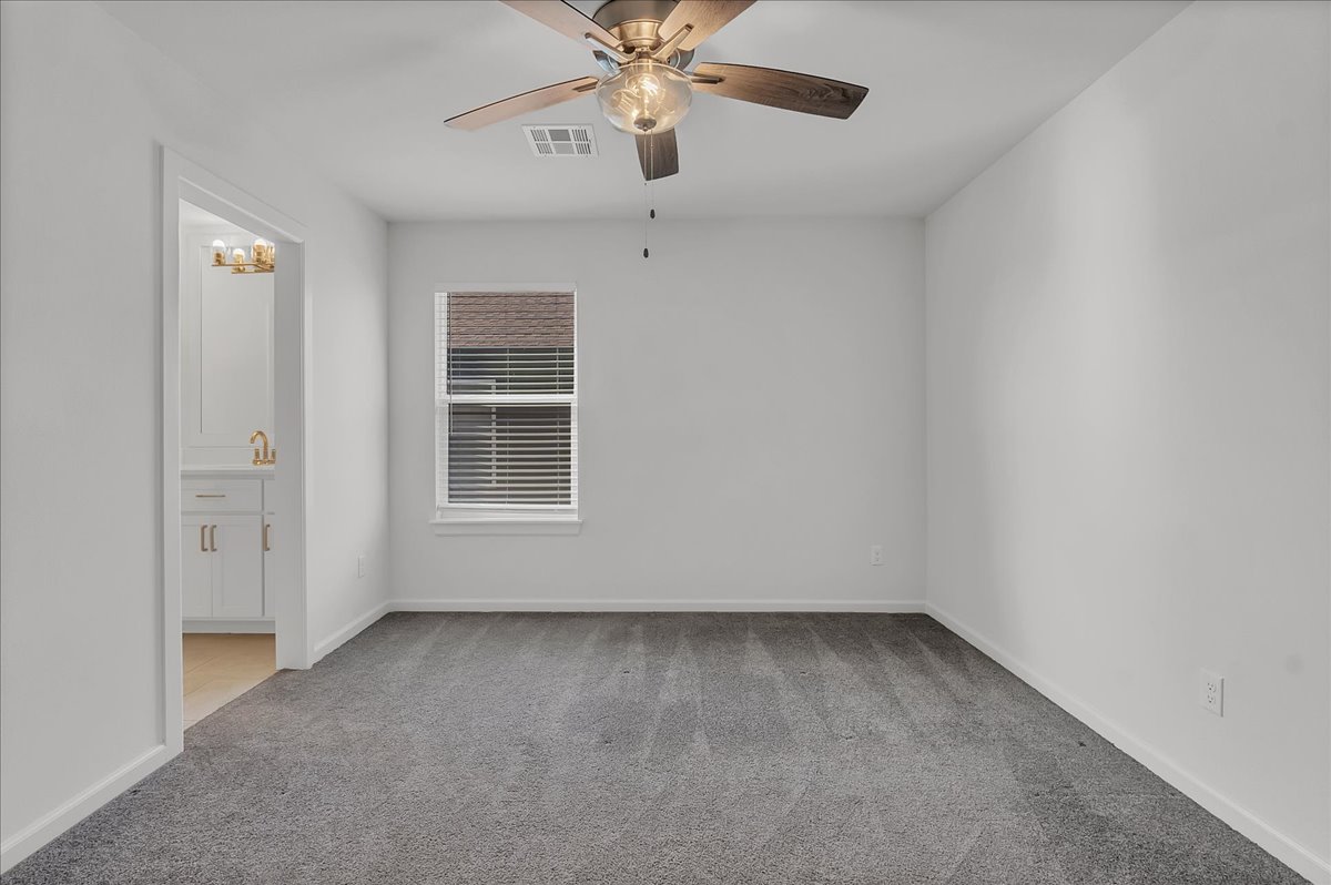 Empty bedroom with gray carpet, a window with blinds, and a ceiling fan.