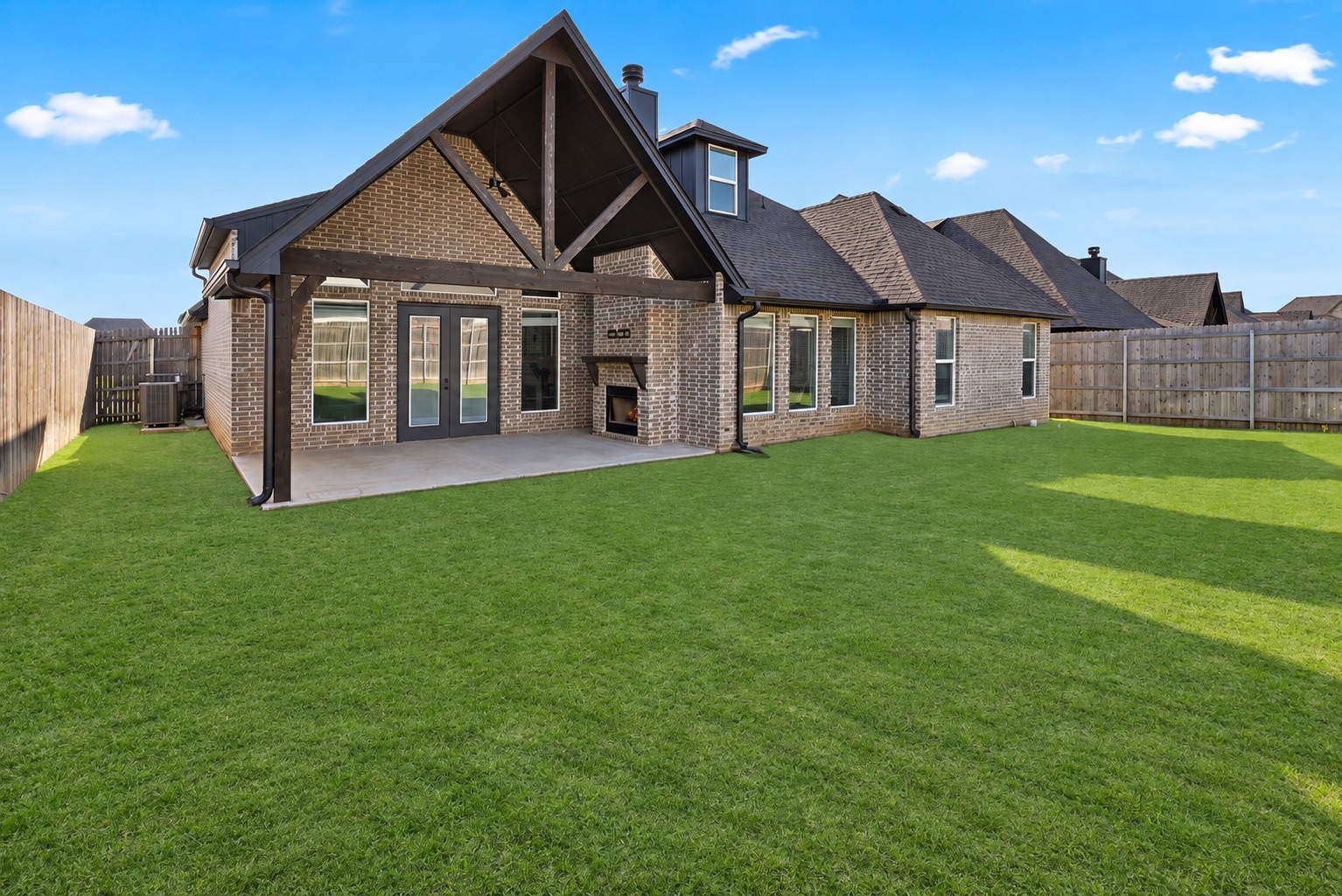Brick home with a covered patio and outdoor fireplace overlooking a spacious fenced lawn.