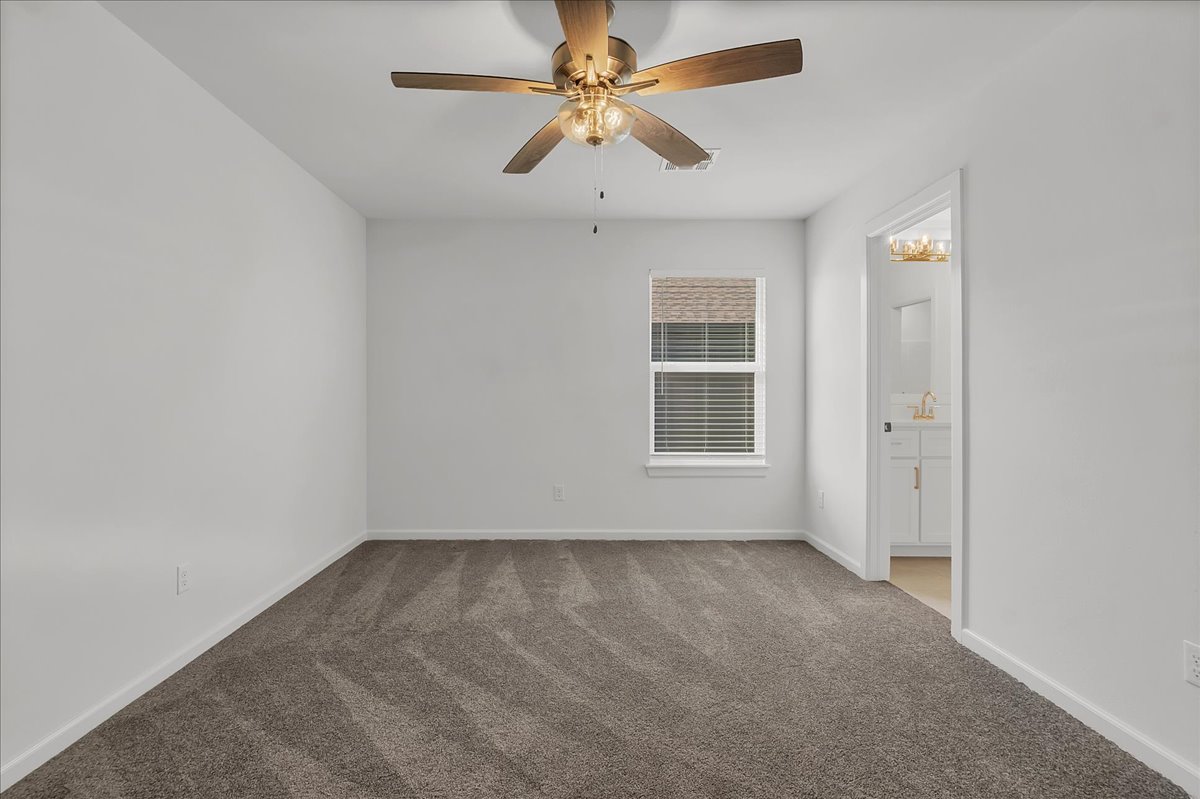 Empty bedroom with gray carpet, a wood-blade ceiling fan, and an adjoining bathroom vanity.