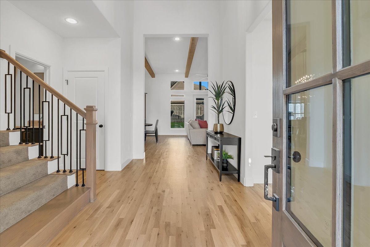 Entry foyer with light wood floors, a carpeted staircase, and a glass-paneled front door.