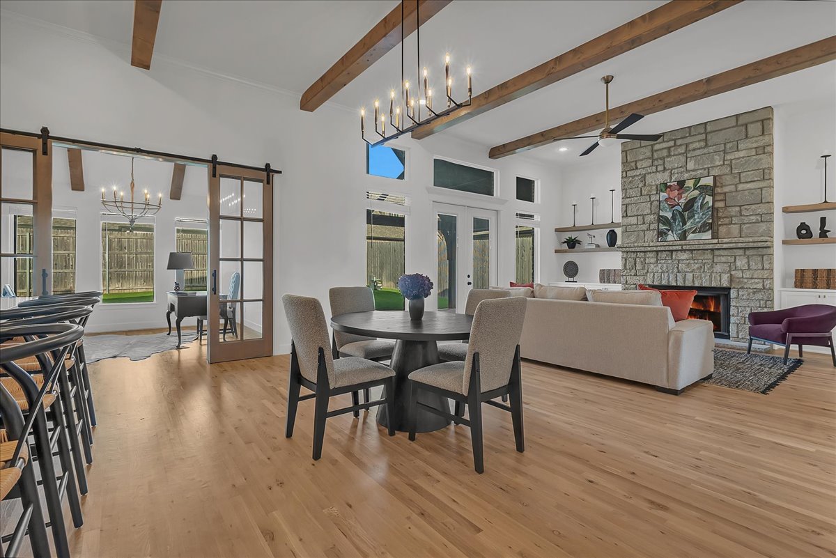Open living and dining room with exposed beams, a stone fireplace, and sliding glass doors to the yard.