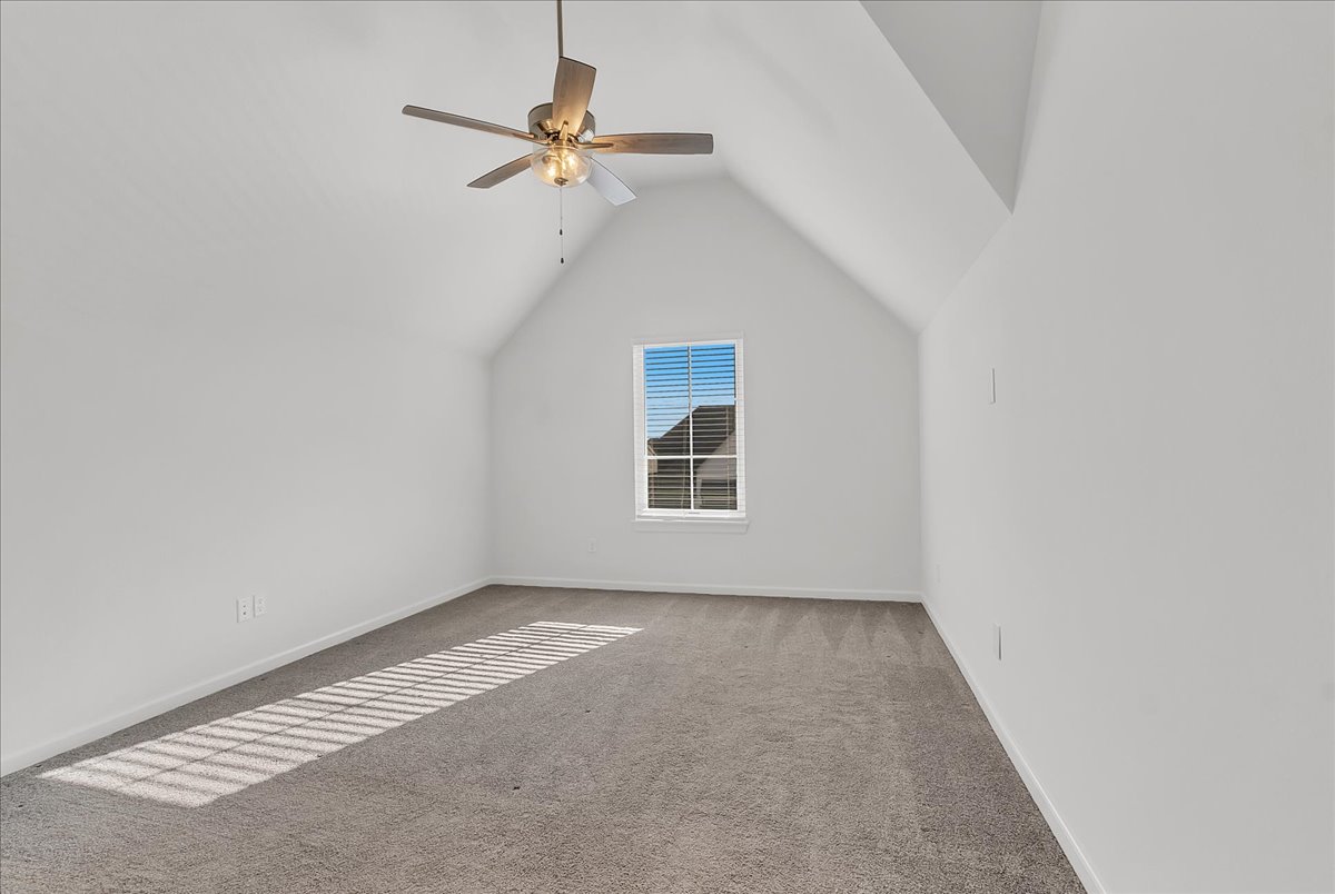 Vacant bedroom with vaulted ceiling, gray carpet, and sunlight casting striped shadows across the floor.