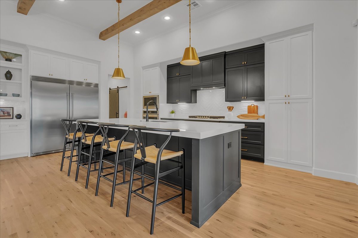 Modern kitchen with a large island, dark cabinets, brass pendant lights, and exposed wood ceiling beams.
