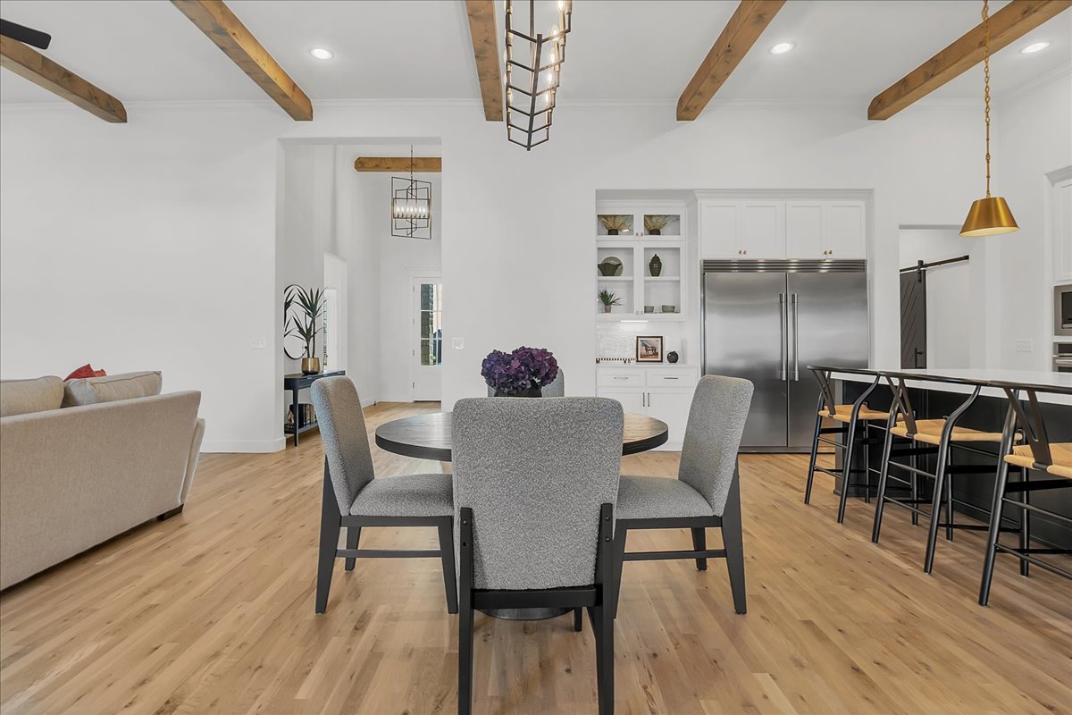 Open-plan dining area with exposed wood beams, round table, and adjoining kitchen.