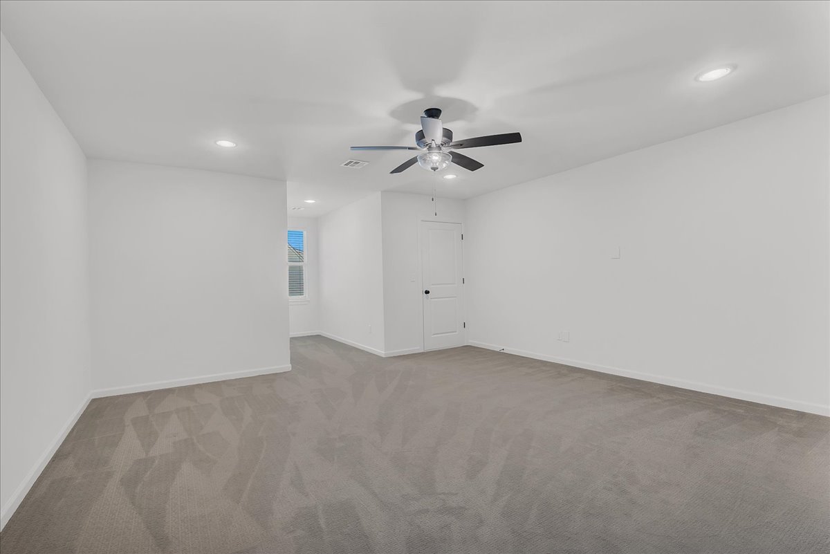 Empty bedroom with gray carpet, ceiling fan, and narrow window beside the door.