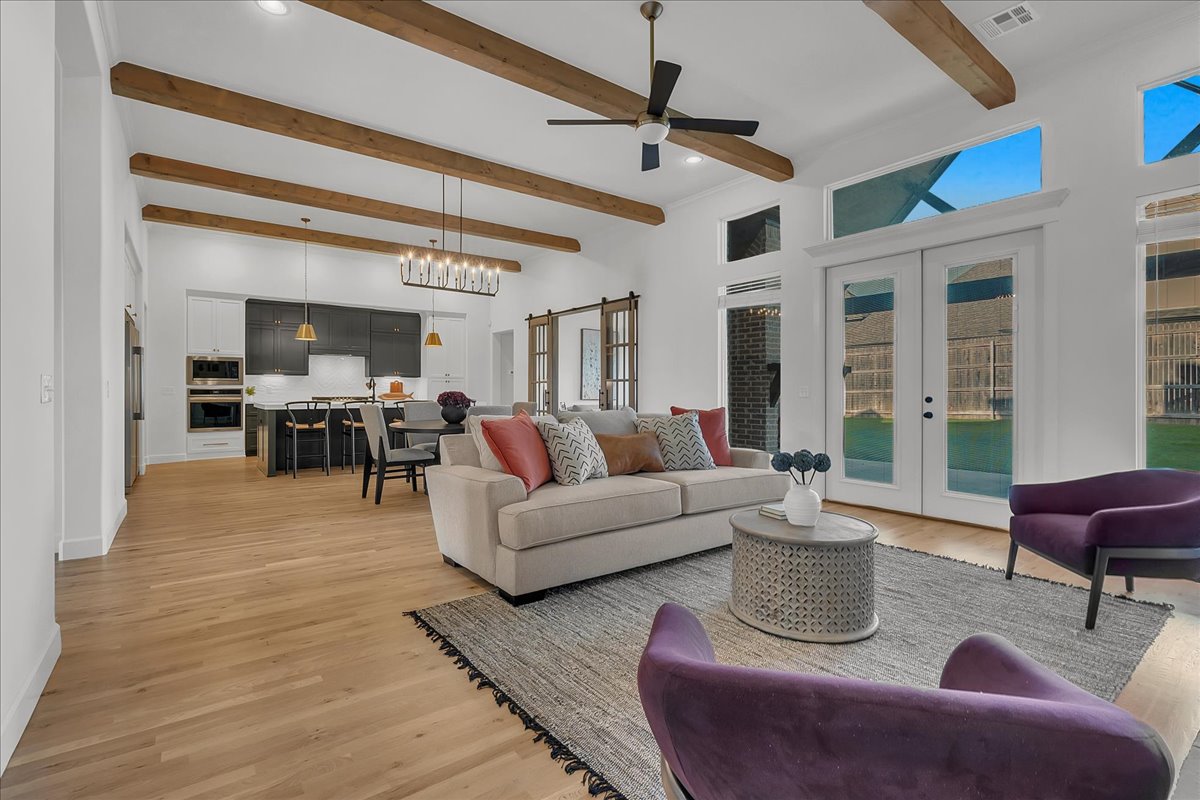 Open-plan living room with exposed wood ceiling beams, staged seating, and glass doors to the backyard.