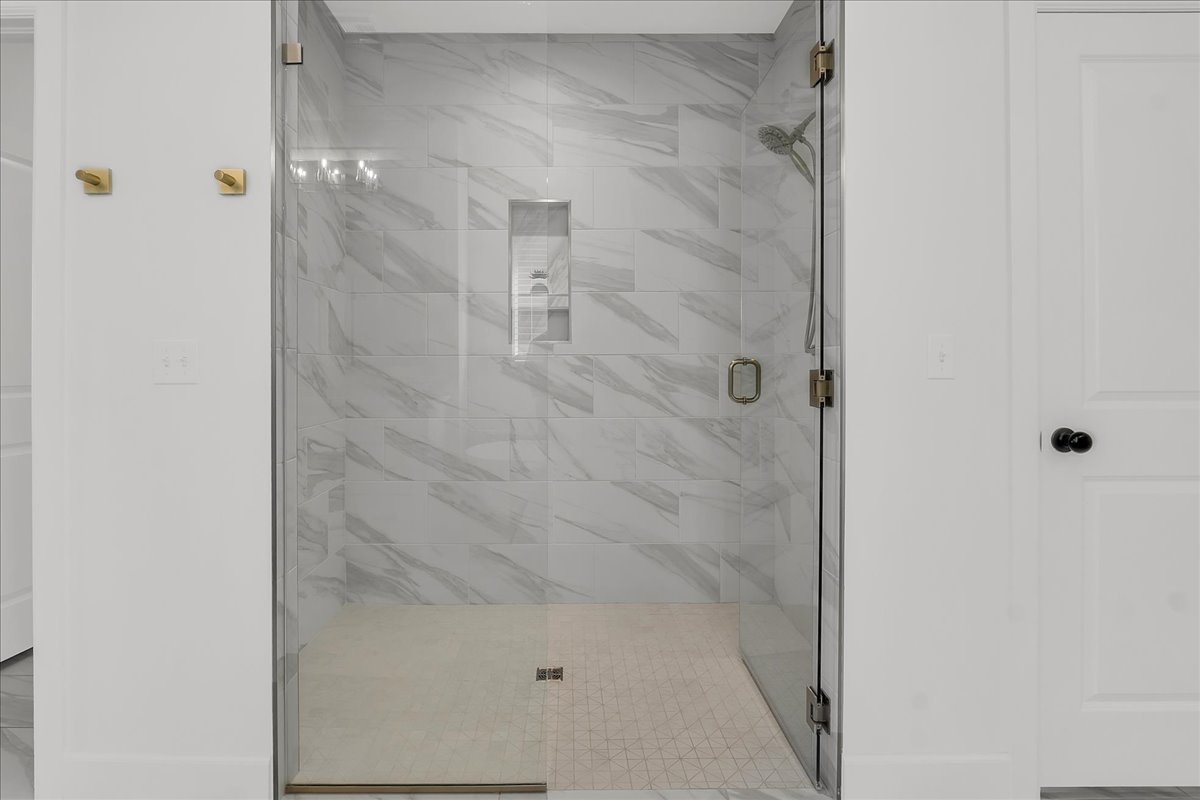 Walk-in shower with marble-look tile walls, a recessed niche, and brass-toned glass hardware.