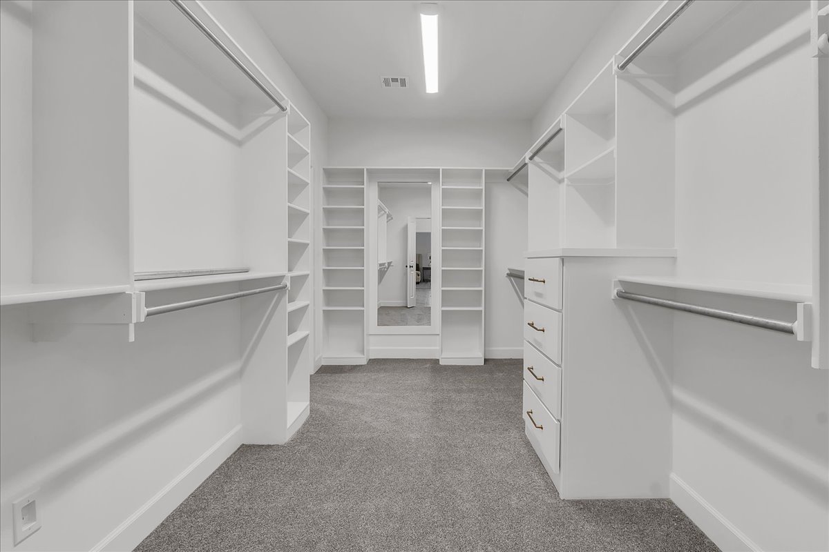 Walk-in closet with white built-in shelves, hanging rods, and a central drawer unit.