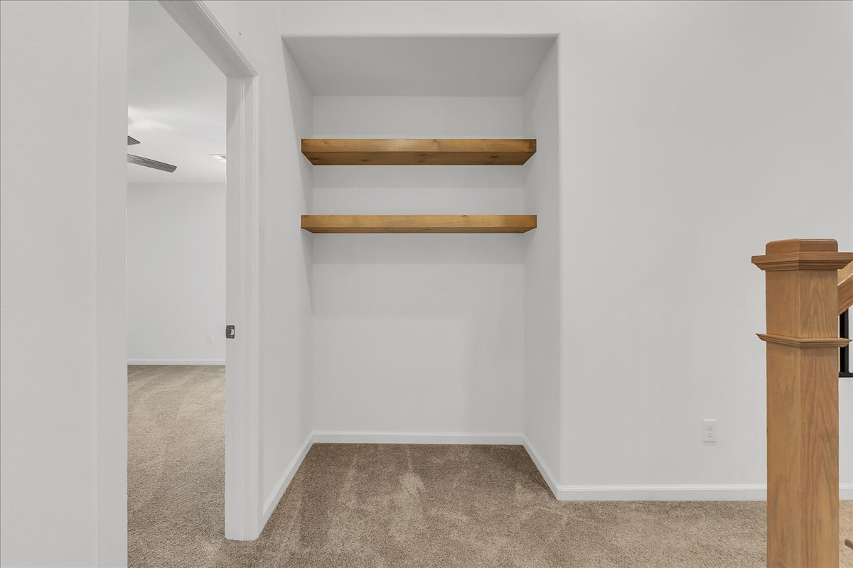 Carpeted alcove with two floating wood shelves beside a staircase.