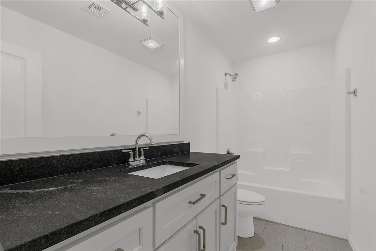 Bathroom with a black stone vanity, large mirror, and white tub-shower combination.