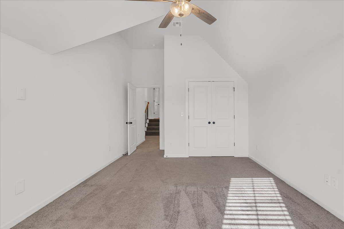 Empty carpeted bedroom with vaulted ceiling, ceiling fan, and double closet doors.