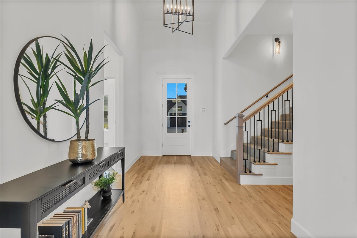 Bright entryway with hardwood floors, a tall front door, and a staircase with black metal railings.