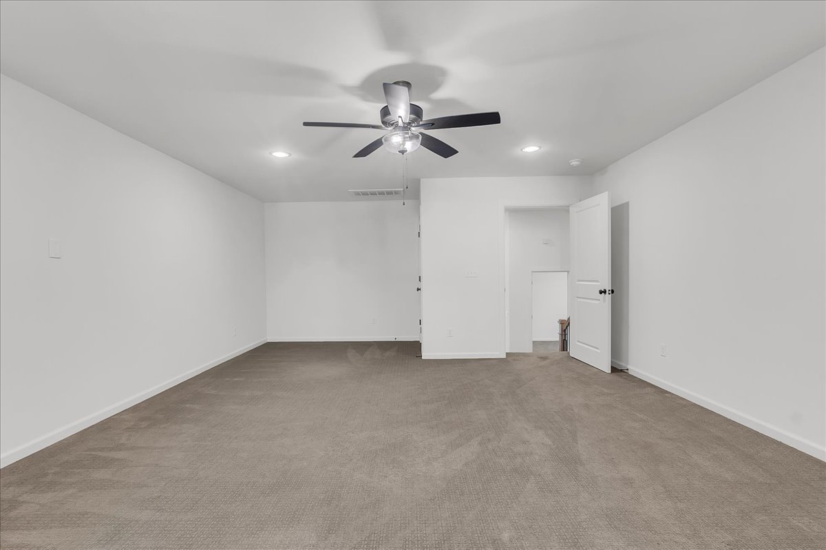 Empty carpeted room with a ceiling fan, recessed lights, and an open doorway.