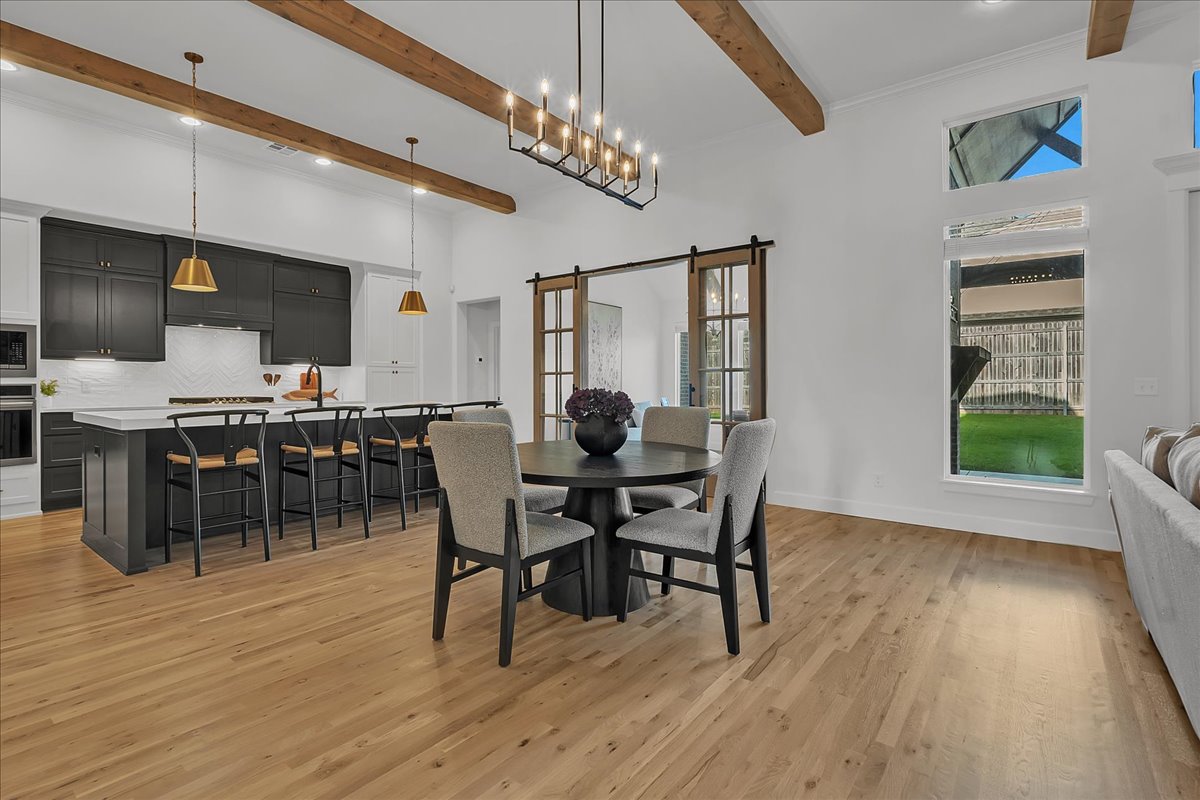 Open kitchen and dining area with dark cabinets, a white island, and exposed wood ceiling beams.