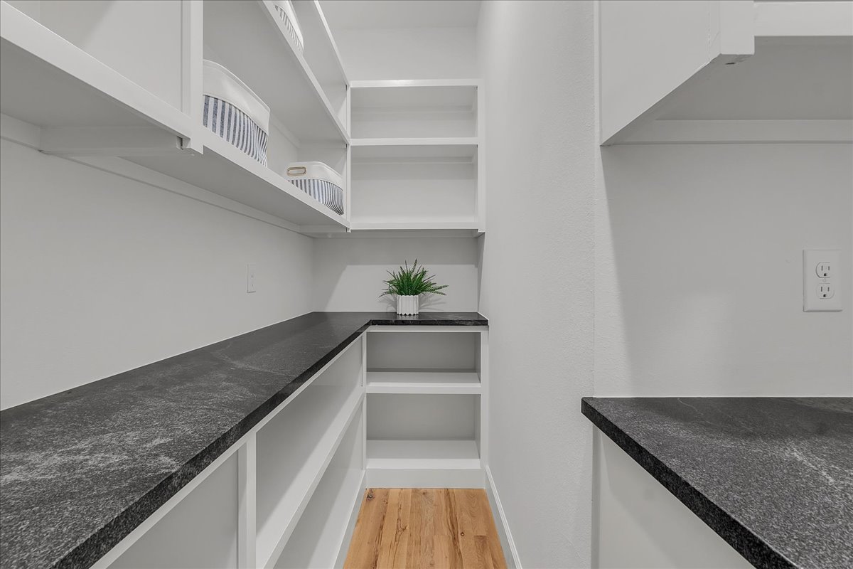 Walk-in pantry with white open shelving, dark stone counters, and a wood plank floor.