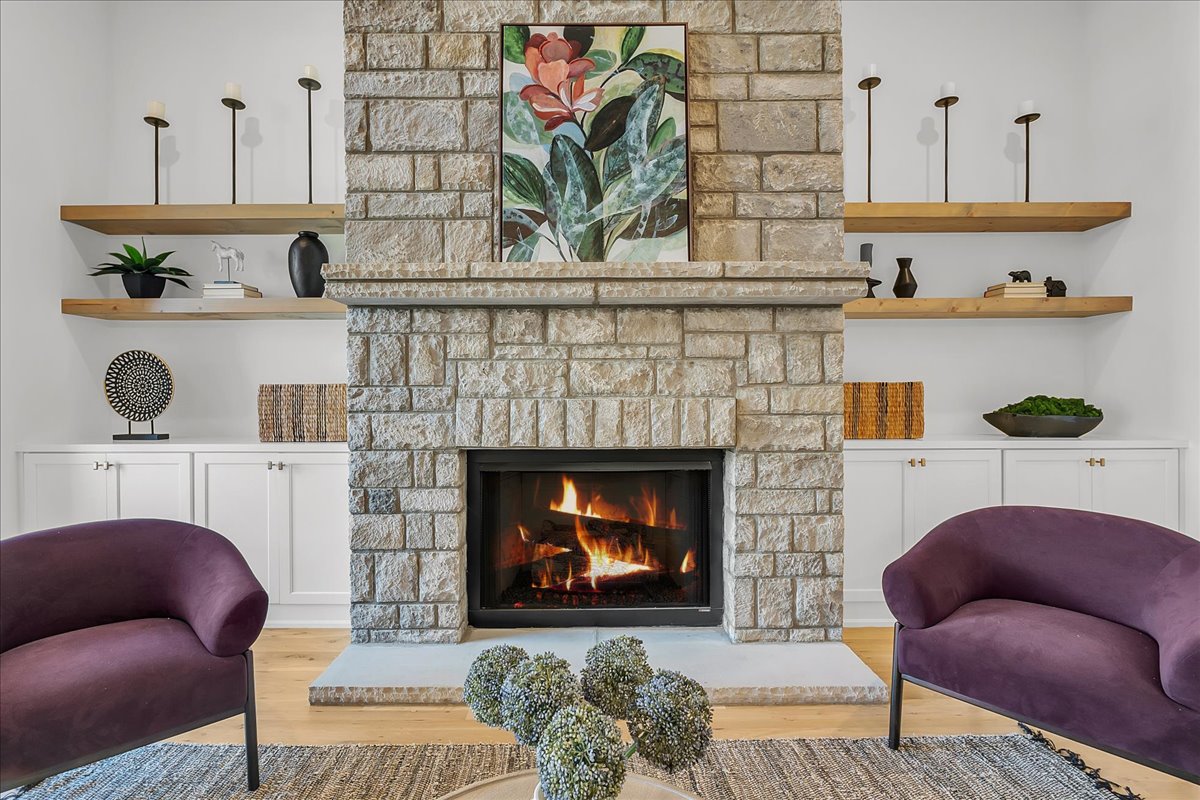 Living room with a lit stone fireplace, built-in shelves, and purple armchairs.