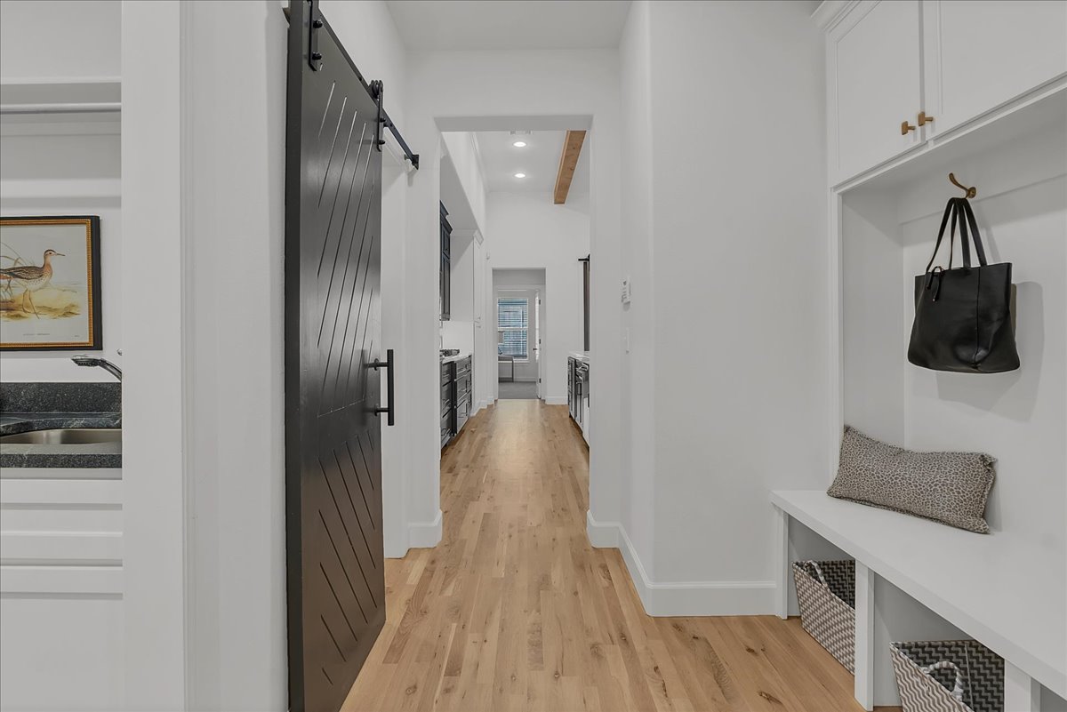 Hallway with light wood floors, a black barn door, and a built-in mudroom bench.