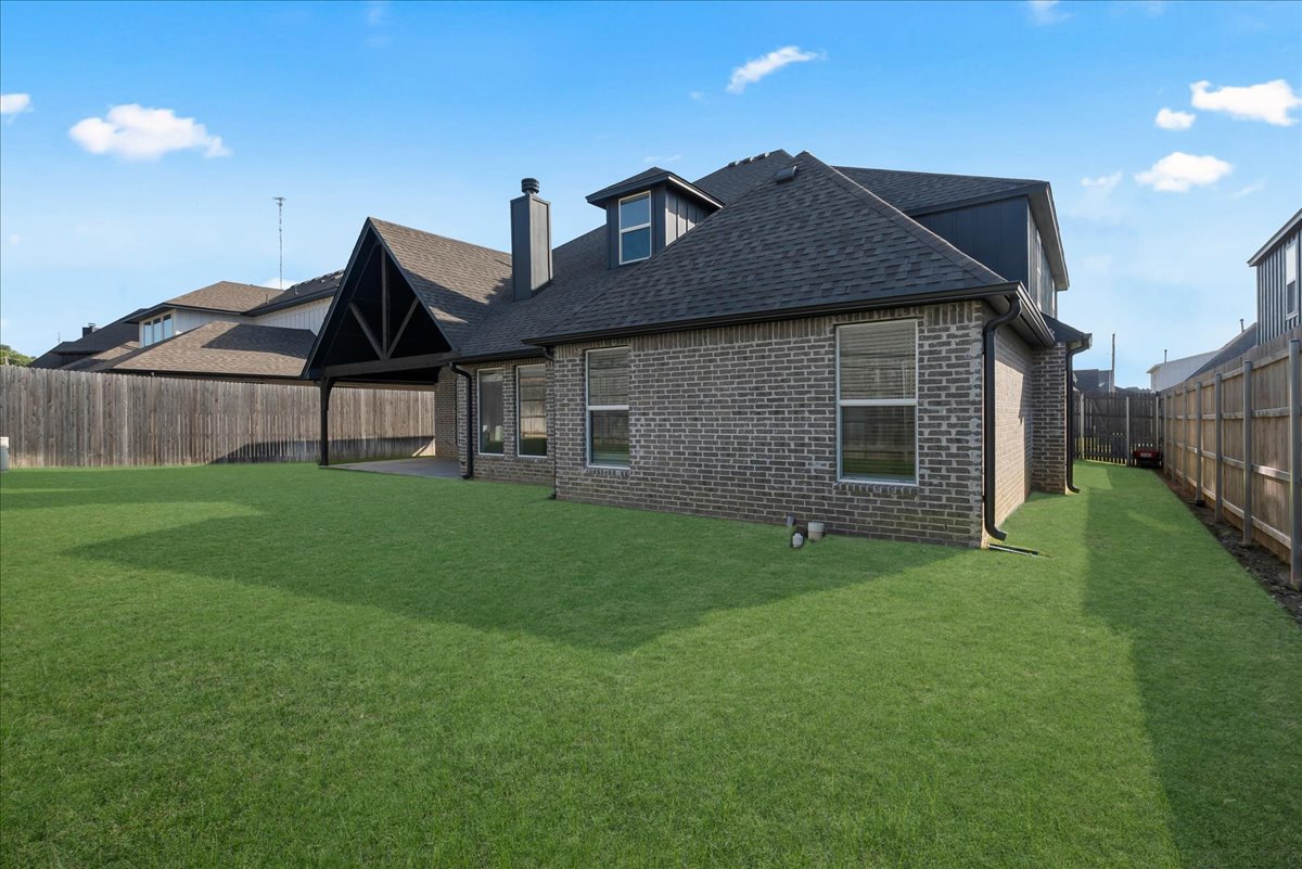 Rear of a brick house with a covered patio and broad fenced lawn.