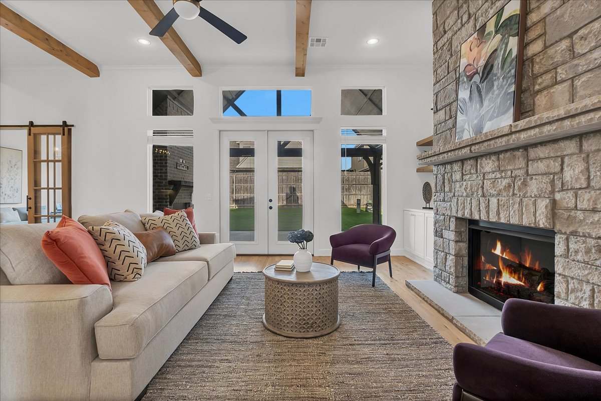 Living room with a stone fireplace, exposed wood beams, and French doors to the backyard.