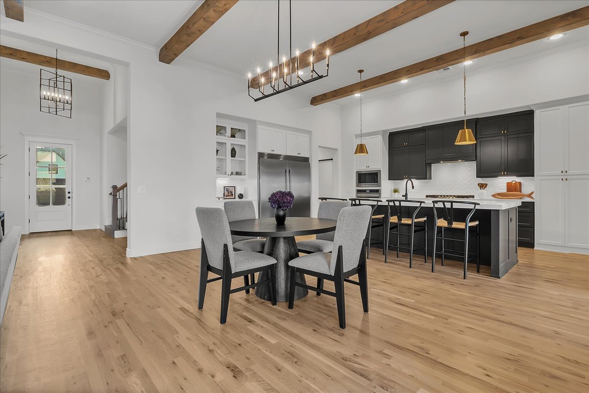 Open kitchen and dining area with a large island, dark cabinetry, and exposed wood ceiling beams.
